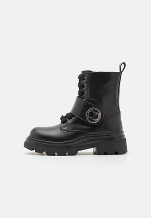 Bota de tobillo de cuero negro con suela gruesa, diseño con cordones, herrajes circulares decorativos y talón reforzado para mayor estabilidad.