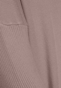Gros plan sur un tissu tricoté rose poudré montrant des sections côtelées et lisses avec des détails de coutures visibles.