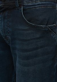 Ciemnoniebieskie dżinsy z widokiem z bliska na teksturę materiału, czterema kieszeniami oraz widocznym metalowym guzikiem w pasie.