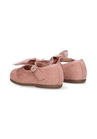 Un par de zapatos de ante rosa para niños pequeños con suelas marrones, hebillas ajustables y lazos de satén decorativos sobre un fondo blanco.