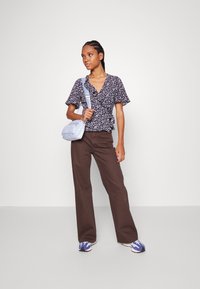 Marineblå blomsterwrap-bluse med korte ærmer, kombinert med brune vide bukser og en lyseblå veske. Sporty blå og hvite joggesko kompletterer antrekket.