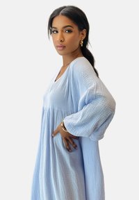 Abito blu chiaro, strutturato, con maniche lunghe e fluide e scollatura a V. Design svasato con vita arricciata, creando una silhouette morbida.