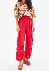 Pantaloni cargo rossi con vita elastica e grandi tasche, abbinati a un top a motivi multicolori con maniche a volant e una vestibilità rilassata.