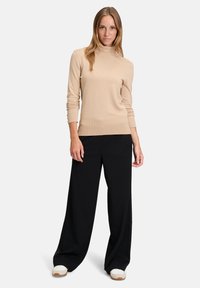 Pull en tricot beige clair à col roulé associé à un pantalon noir à jambes larges et des baskets blanches, avec des poignets et un ourlet côtelés.