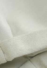 Ljusgrått tyg med en mjuk, stickad textur; har en ribbad midja och sömmar som visar mjuka fibrer och subtila sömnadsdetaljer.