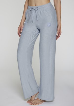 Woman wearing light blue wide-leg lounge pants with elastic waistband and drawstring, standing barefoot against a plain background.