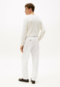 Camicia bianca a maniche lunghe, tessuto leggero, vestibilità slim. Abbinata a pantaloni bianchi larghi, due tasche posteriori con bottoni, e scarpe scure.
