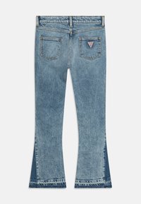 Pantalones de mezclilla de campana en azul claro con cintura alta, que cuentan con bolsillos traseros y un parche de logo triangular en el bolsillo derecho.