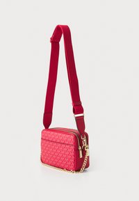 Geantă crossbody roșie cu accente aurii, realizată dintr-un material texturat cu un model de logo 'MK', închidere cu fermoar și curea metalică detașabilă.