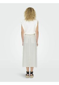 Top blanco sin mangas combinado con una falda larga de color claro a rayas que presenta dos bolsillos traseros y un diseño recto y fluido. Sandalias negras.