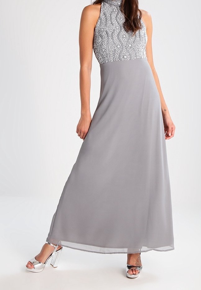 Gray maxi dress with a fitted patterned bodice and a flowing skirt. Features a mock neck and is paired with metallic high-heeled sandals.