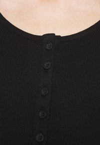 Svart räffladtank topp med rund halsringning, med en sexknaps knäppning fram och textilstruktur.