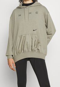 Přehnaně velká mikina s kapucí v olivově zelené barvě z bavlněné směsi s černými logy Nike. Obsahuje texturovanou, elastickou kapsu a volný střih.