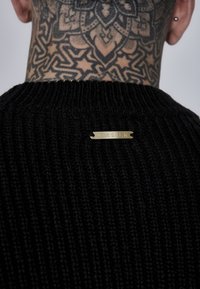 Czarny sweter z prążkowanego dzianiny z okrągłym dekoltem. Złota metka "SIKSILK" na tylnej stronie dekoltu. Gładka tekstura i dopasowany krój.