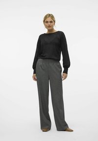 Sort tekstureret langærmet top kombineret med løstsiddende, gråmønstret bukser. Modellen bærer brune sko. Enkel, minimalistic design.