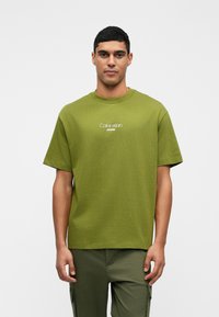 Zelena pamučna majica s okruglim izrezom, kratkim rukavima i bijelim logom "Calvin Klein JEANS" na prednjem dijelu. Ima opušteni kroj.