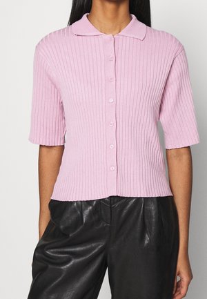Cárdigan de manga corta rosa con relieve, cuello con solapa y cierre de cinco botones, combinado con pantalones de cuero negros.