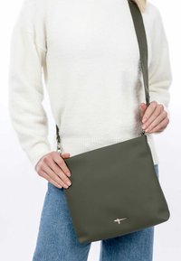 Borsa a tracolla verde con texture liscia e design minimalista, con un accento argentato. Presenta una tracolla lunga regolabile e una chiusura sicura.