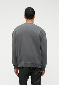 Γκρι φούτερ με χαλαρή εφαρμ�ογή, στρογγυλή λαιμόκοψη και μακριά μανίκια. Φτιαγμένο από μαλακό ύφασμα, με ριμπ τελείωμα και μανσέτες.