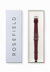Orologio con cassa quadrata e cinturino in pelle maroon, hardware argentato e quadrante minimalista. Presentato in una scatola bianca con marchio e interno beige.