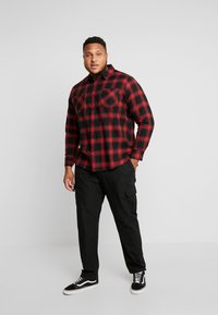 Rood en zwart geruit overhemd met lange mouwen, twee borstzakken; gecombineerd met zwarte cargobroek en zwarte sneakers met witte zolen.