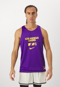 Lila kosárlabda mez hálós anyagból, sárga "LOS ANGELES LAKERS" felirattal és Nike logóval. Fehér rövidnadrággal viselve.