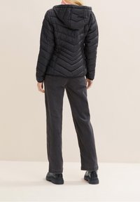 Černá prošívaná péřová bunda s kapucí a vzorem rybí kostry. Kombinována s tmavými širokými kalhotami a černými botami.