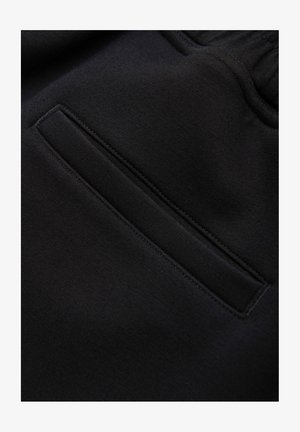 Gros plan d'une poche de sweat à capuche en tissu noir avec des coutures visibles et une taille élastiquée à cordon.