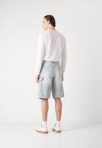 Şorturi din denim de culoare albastru deschis, cu un fit relaxat, buzunar lateral tip cargo și tiv desfăcut. Asortate cu o bluză albă cu mânecă lungă și adidași.