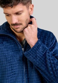 Chaqueta de forro polar azul marino con cremallera frontal, que presenta un patrón texturizado y acolchado, así como un collar alto. Material suave y esponjoso.