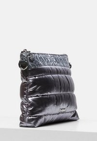 Metaliczna srebrna pikowana torebka z szarą klapą w wzory, wyposażona w górne zamknięcie na suwak oraz regulowany pasek na ramię.