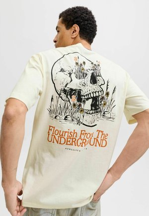 Cremefarbene Baumwoll-T-Shirt mit einem großen schwarzen Totenkopf-Design, umgeben von Blumen, und oranger Schrift mit dem Text "Flourish From The UNDERGROUND."