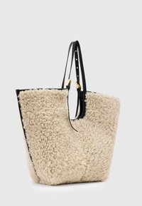 Zandkleurige, gestructureerde nepsherling handtas met zwarte leren accenten en verstelbare bandjes. Voorzien van een ruime open bovenkant en gouden hardware.