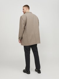 Abrigo de mezcla de lana gris con un corte estructurado y cuello con muescas, emparejado con pantalones y zapatos negros, visto desde atrás.