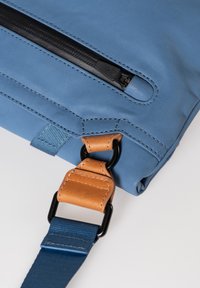 Borsa in tessuto blu con tasca con zip, connettore in pelle e tracolla in tessuto blu. I dettagli cuciti accentuano il design.