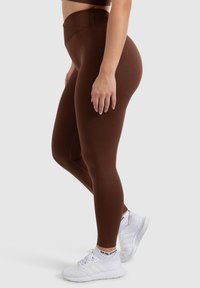 Bruine high-waisted leggings van rekbaar materiaal, aangesloten ontwerp, gladde textuur, gecombineerd met witte sportschoenen.
