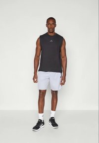 Top de sport sans manches noir avec un logo subtil, associé à un short de sport gris clair. Des chaussures d'entraînement noires et des chaussettes blanches complètent la tenue.