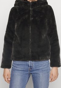 Chaqueta de piel sintética negra con capucha, cierre de cremallera, textura suave y mangas largas, combinada con jeans azul claro.