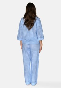 Vaaleansininen pyjamapuku, jossa on geometrinen kuvio, pitkät hihat, löysä istuvuus sekä käänteet ylhäällä ja alhaalla lisämukavuutta varten.