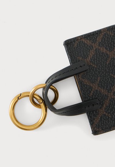 Porte-clés en cuir noir texturé avec motif marron, attaché à deux anneaux métalliques dorés entrelacés sur fond blanc.