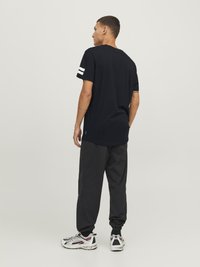 Camiseta de algodón negra de manga corta con dos franjas blancas. Combinada con pantalones negros holgados y zapatillas blancas.