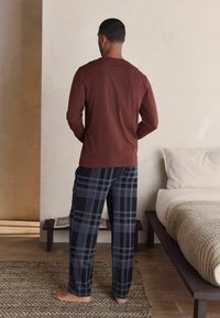 Langärmliges braunes Hemd und schwarze karierte Schlafanzughose. Von hinten gesehen. Weicher Stoff, lockere Passform, schlichtes Design und keine sichtbaren Muster.