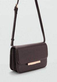 Brązowa torba typu crossbody z faux skóry, z klapą i różowo-złotą listwą akcentującą. Posiada długi, regulowany pasek oraz prostokątny kształt.