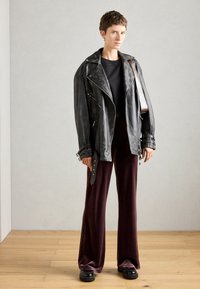 Μαύρο δερμάτινο μπουφάν μηχανής με τσέπες με φερμουάρ, συνδυασμένο με μπορντώ παντελόνι σε φαρδιά γραμμή και χοντρές μαύρες πλατφόρμες. Λείο υφάσμα.