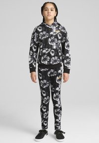 Svart blommig hoodie med vita och grå blommönster, matched med leggings. Har en guldlogotyp och huva. Svarta sneakers.