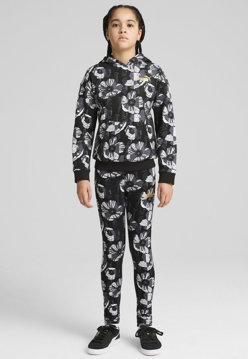 Svart blommig hoodie med vita och grå blommönster, matched med leggings. Har en guldlogotyp och huva. Svarta sneakers.