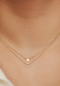 Colliers superposés en ton or, présentant un petit cœur solide et un pendentif en forme de grand cœur orné de pierres claires.