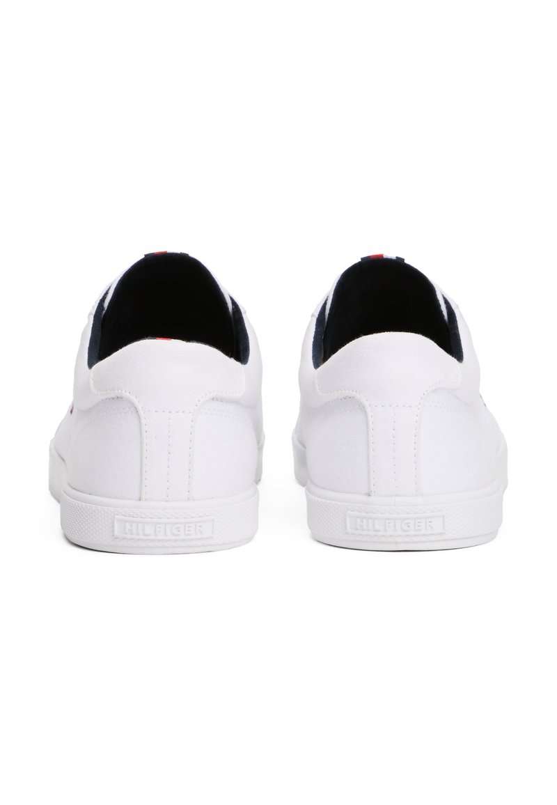 Zapatillas de lona blancas con una textura suave, que presentan un interior azul marino y sutiles acentos rojos en el talón. Suela de goma con branding.