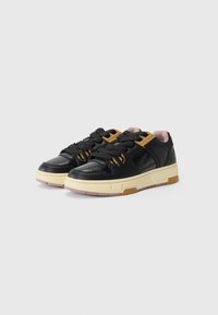 Black sneakers with smooth leather upper, yellow accents, and thick cream midsole. Features round laces and perforated toe for breathability.