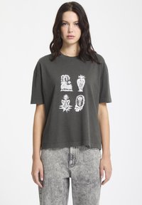 Camiseta de algodón gris oscuro con mangas cortas, con diseños gráficos blancos en un patrón cuadrado en la parte frontal, de corte relajado.